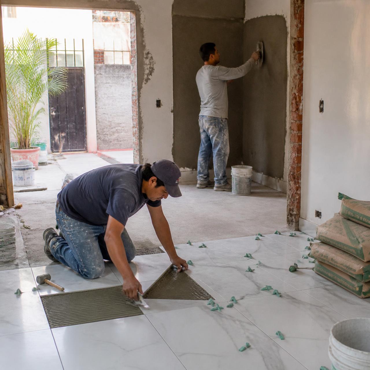 Trabajadores colocando piso y aplanando muros en una remodelación.